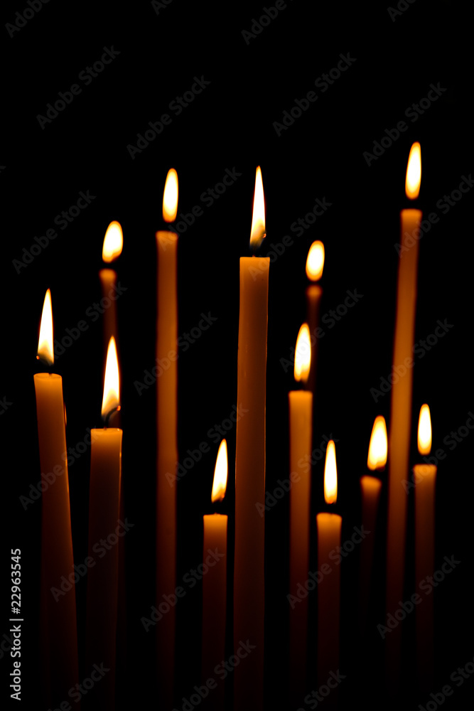 Dozen of long lighted candles on a black background