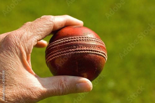 Used red leather cricket ball being held by hand