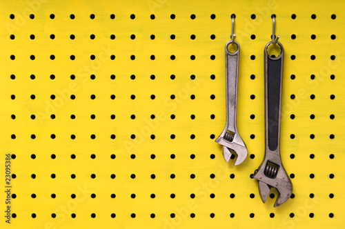 Two wrenches hang from hooks on yellow pegboard photo