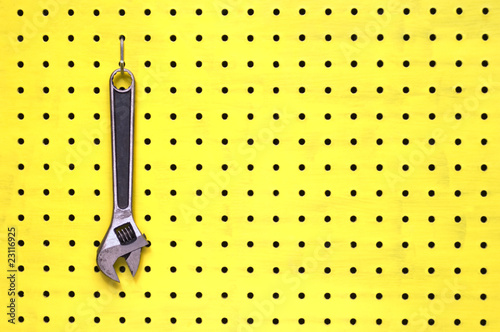 One adjustable wrench hangs from a hook on yellow pegboard photo