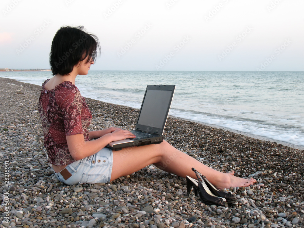 young woman using laptop on a beach