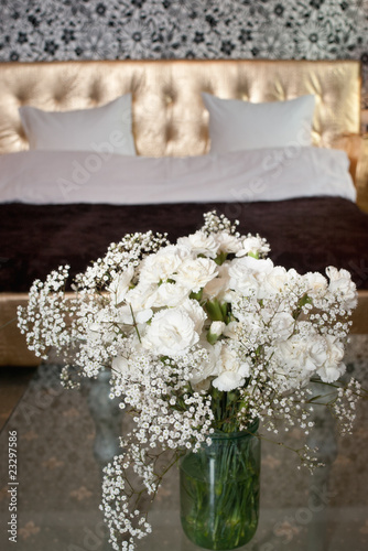 White fresh flowers in bowl with blurred bed with two pillows