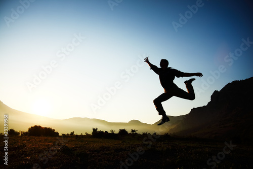 Silhouette of a young male jumping over sunset background with copyspace