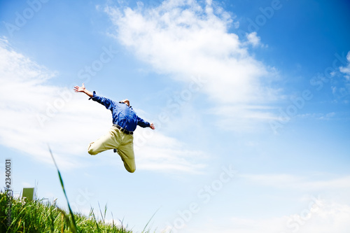 Businessman jumping on a green meadow with copyspace