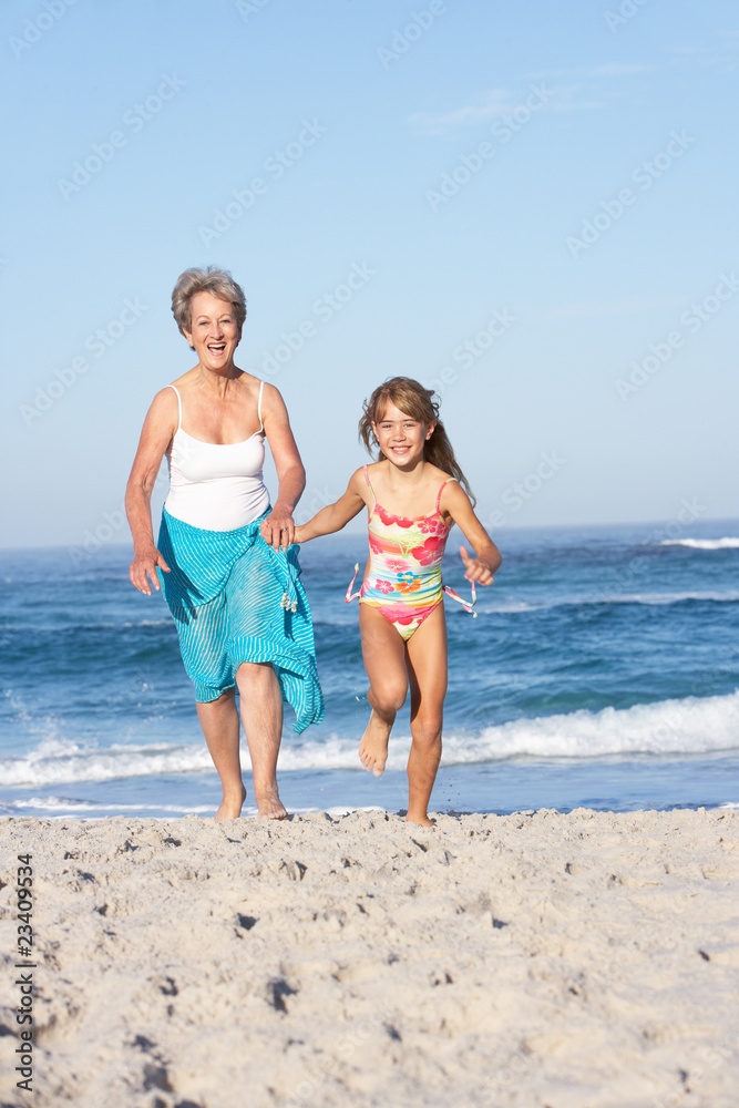 Naklejka premium Grandmother Running With Granddaughter Along Sandy Beach