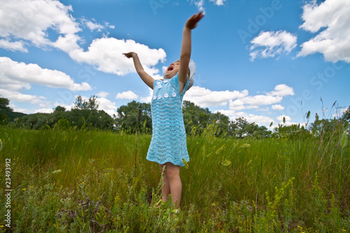Cute little girl rising hands in a grass field