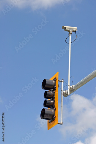 Security camera with traffic light and blue sky background.