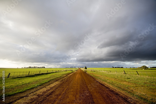 Beautiful red dirt road in the country stretching off into the distance under a stormy sky with sunlight filtering through in country Australia