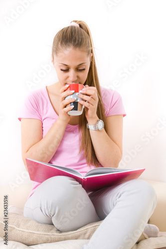 Young girl holding a cup and reading book on sofa photo