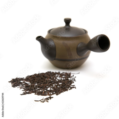 small individual ceramic teapot and scattered tea leaves on whit