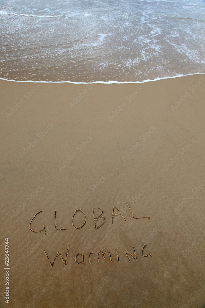 Fototapeta premium Global warming written in the sand at beach with rising wave