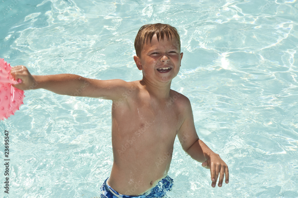 young boy plays with ball in pool