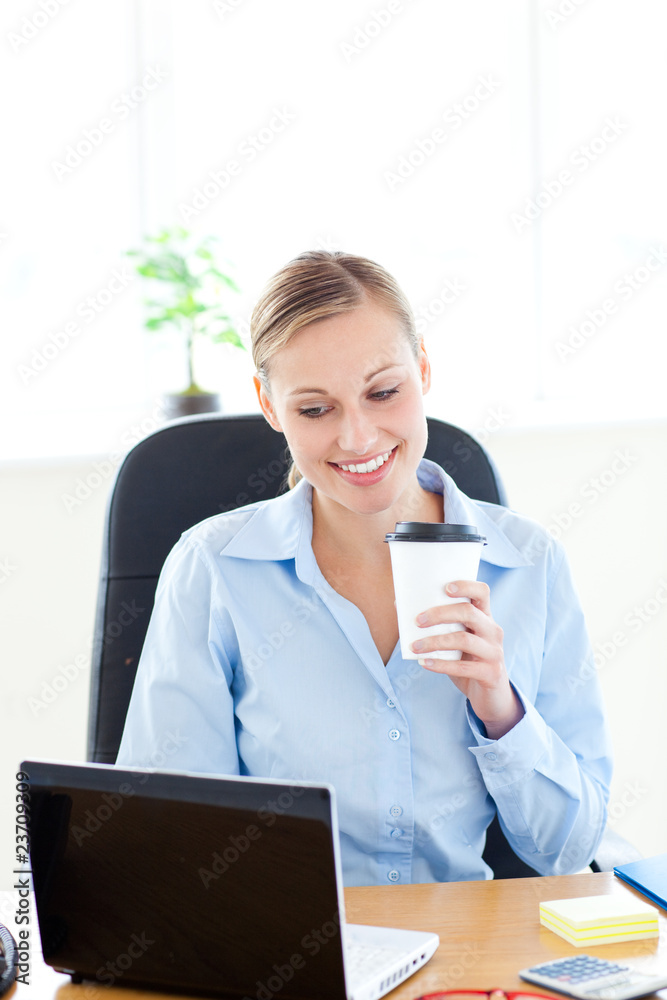 Smiling businesswoman holding a coffee while using a laptop Smiling businesswoman holding a coffee while using a laptop