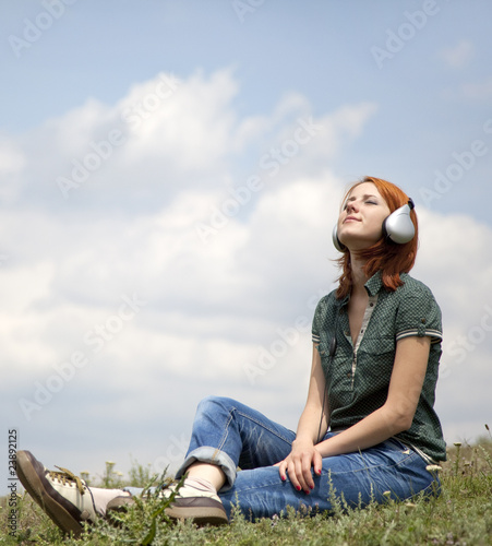 Young smiling girl with headphones sitting at green grasss. photo