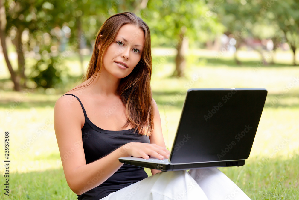 Beautiful young woman sits on a grass in a park with the laptop. Beautiful young woman sits on a grass in a park with the laptop.