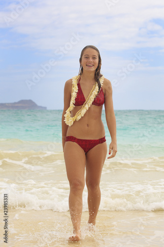 pretty teenage girl walk out of the ocean with a flower lei