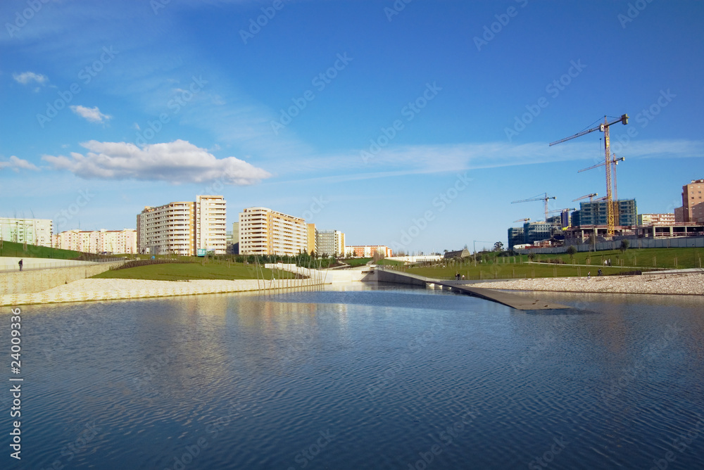 Apartment buildings, construction site, green park over lake