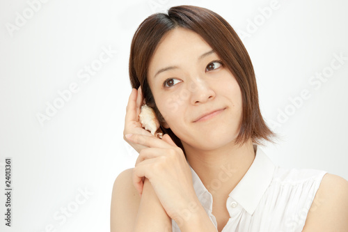 貝を耳にあてる女性