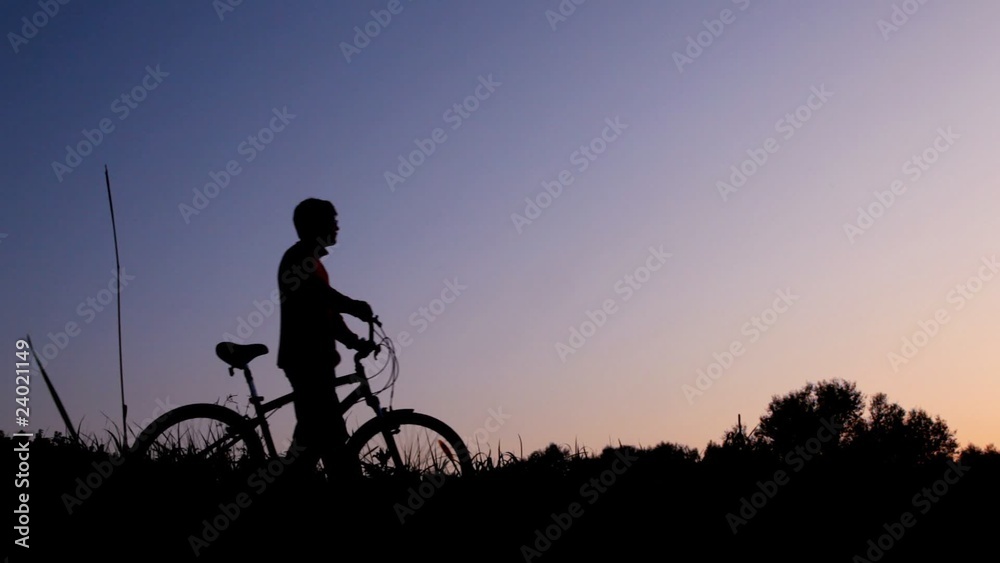 man walking with bicycle against sunset sky man walking with bicycle against sunset sky