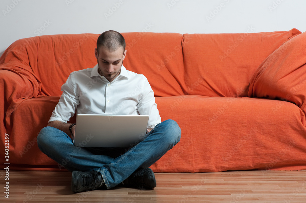 uomo seduto vicino a divano arancione che lavora al computer