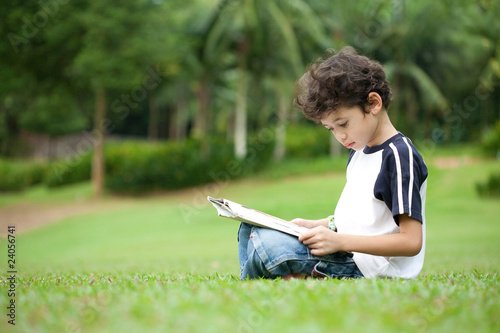 Young boy enjoying his reading book in outdoor park