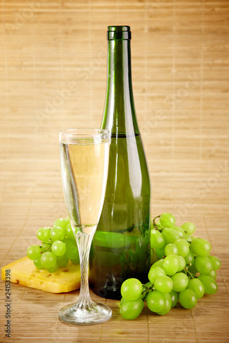 Bottle and glass of white wine with cheese and grapes