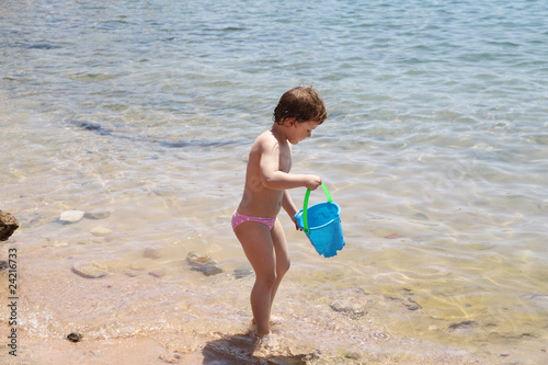 Four years old girl with the blue bucket on the sea