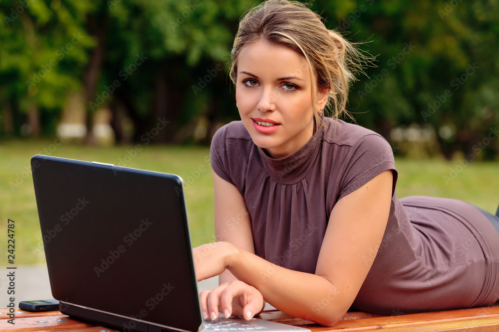 Young pretty woman with laptop lying on the bench in a park