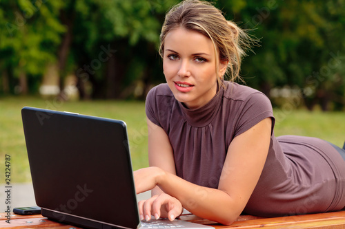 Young pretty woman with laptop lying on the bench in a park