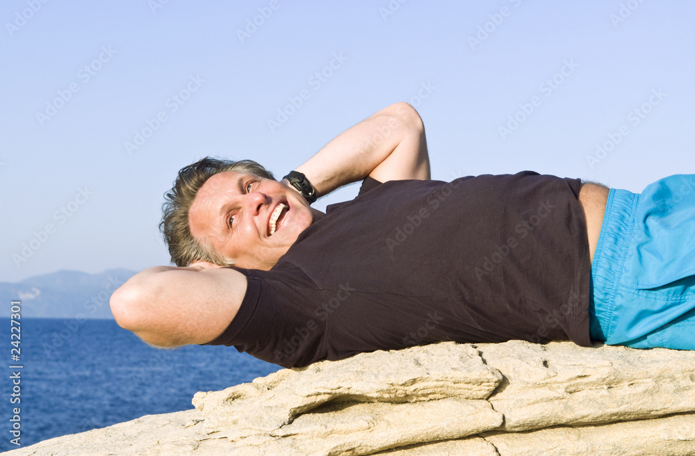 A happy smiling man in his forties laying on a rock