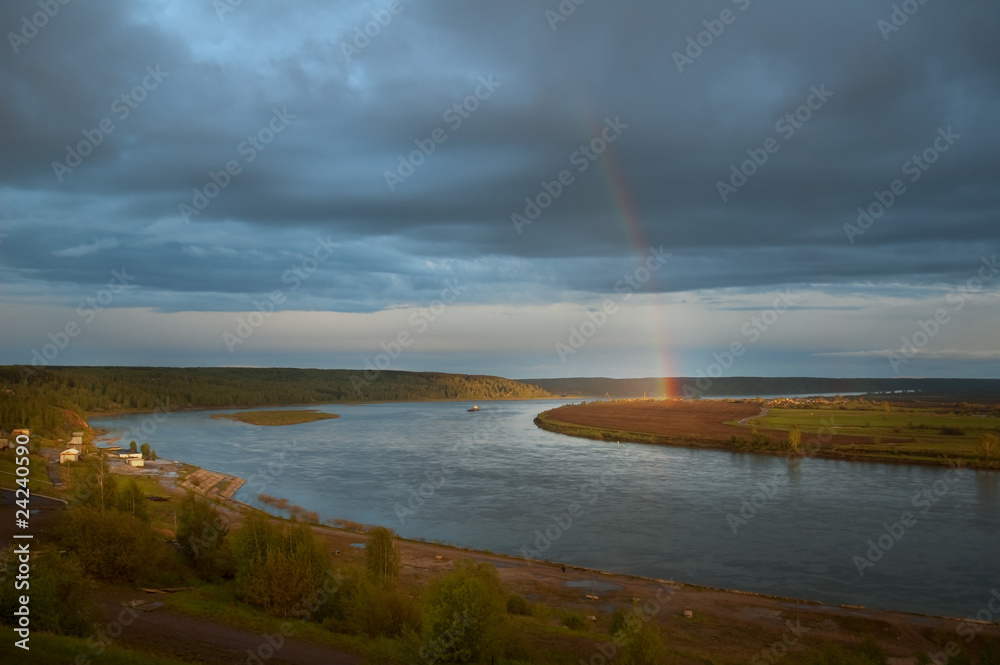 Rainbow on a distant river bank lights all around.