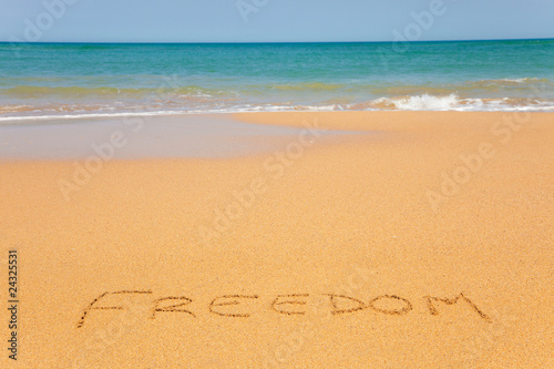 Word "Freedom" written on beach sand with wave approaching