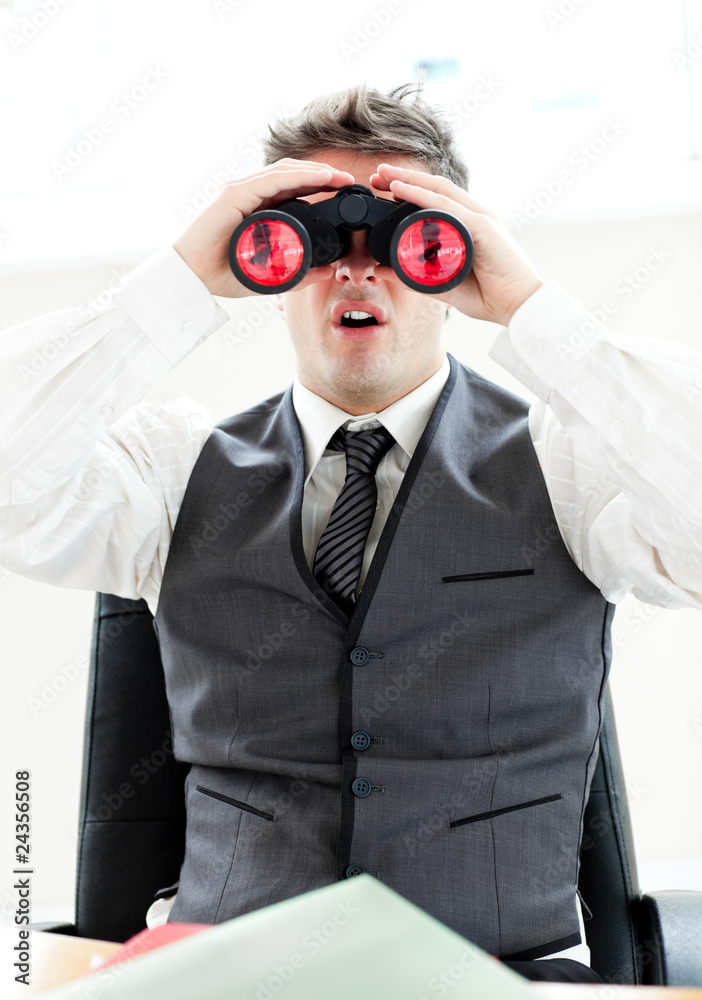 Impressed businessman looking through binoculars sitting in his Impressed businessman looking through binoculars sitting in his