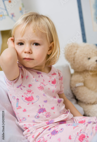 little girl in bed touching ear