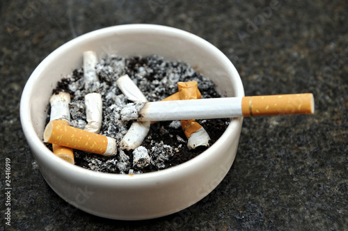 Dirty glass ashtray with butts and burning cigarette