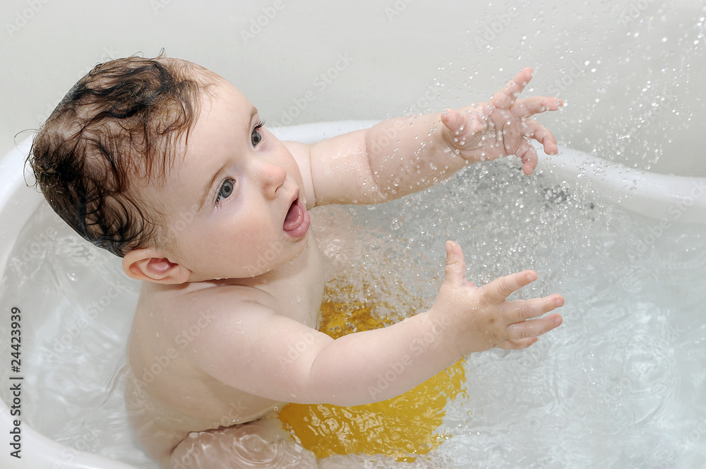 Fototapeta premium Cute baby playing with water in white tub