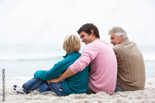 Grandfather, Father And Grandson Sitting On Winter Beach