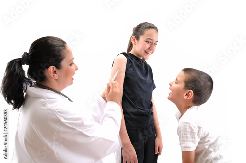 Doctor giving an injection to a teenager, her brother laughing.