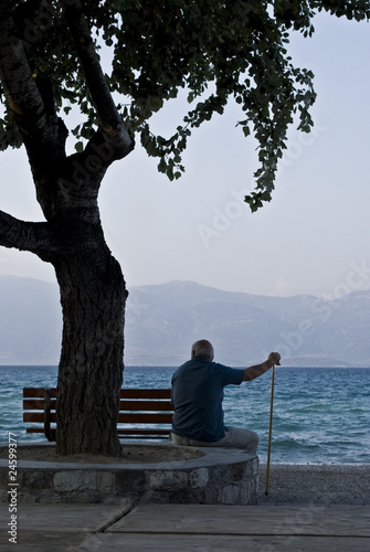 An old man sitting behind a bench and gazing at the sea