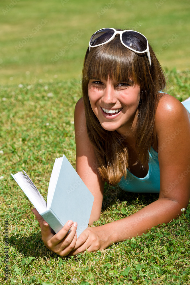 Smiling young woman lying down on grass with book Smiling young woman lying down on grass with book