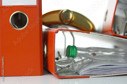 Alkohol am Arbeitsplatz - Versteckte Schnapsflaschen im Aktenordner und ein Flachmann als Symbol für Sucht im Büro 