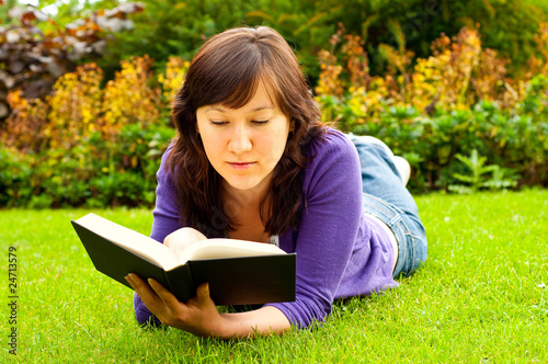 young woman lying on the grass and reading a book in a park
