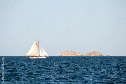 small yacht sailing on the sea with island in the background .