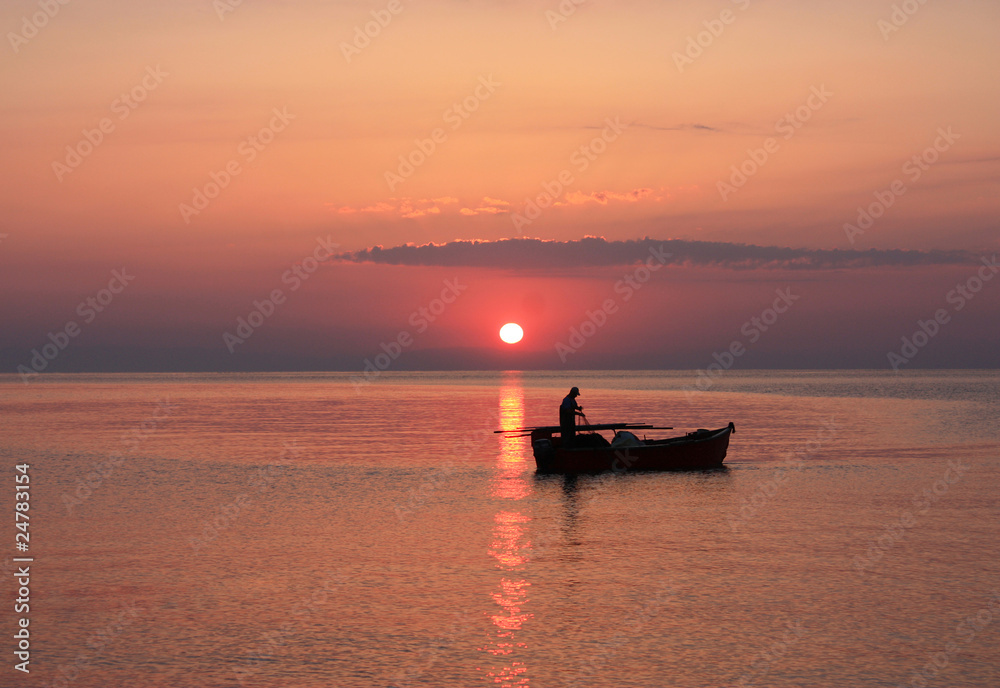 The setting sun silhouettes fishermen in a boat