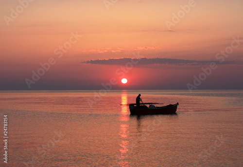 The setting sun silhouettes fishermen in a boat