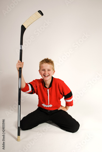 handsome young boy in hockey uniform kneeling with hockey stick