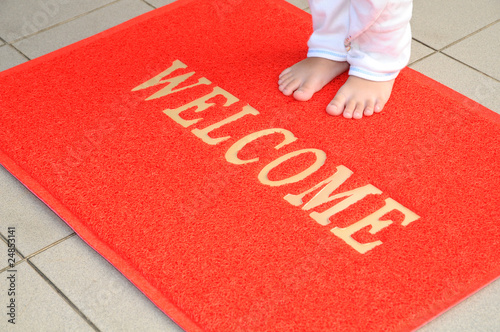 Child Standing On A Red Welcome Mat