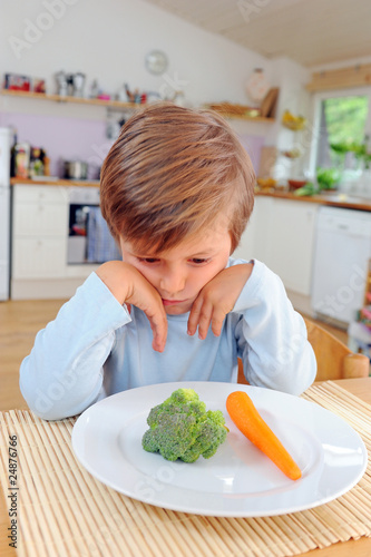 Kind sitzt vor Teller mit Gemüse