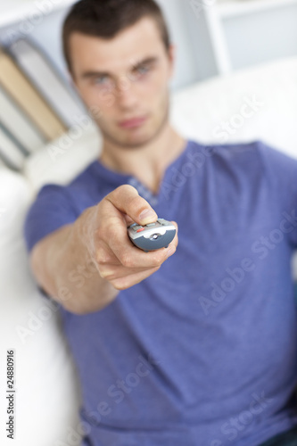 Serious young man holding a remote sitting on the sofa