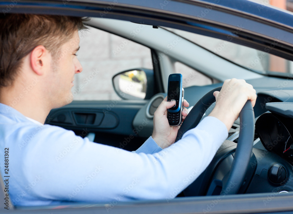 Positive young man sending a text while driving